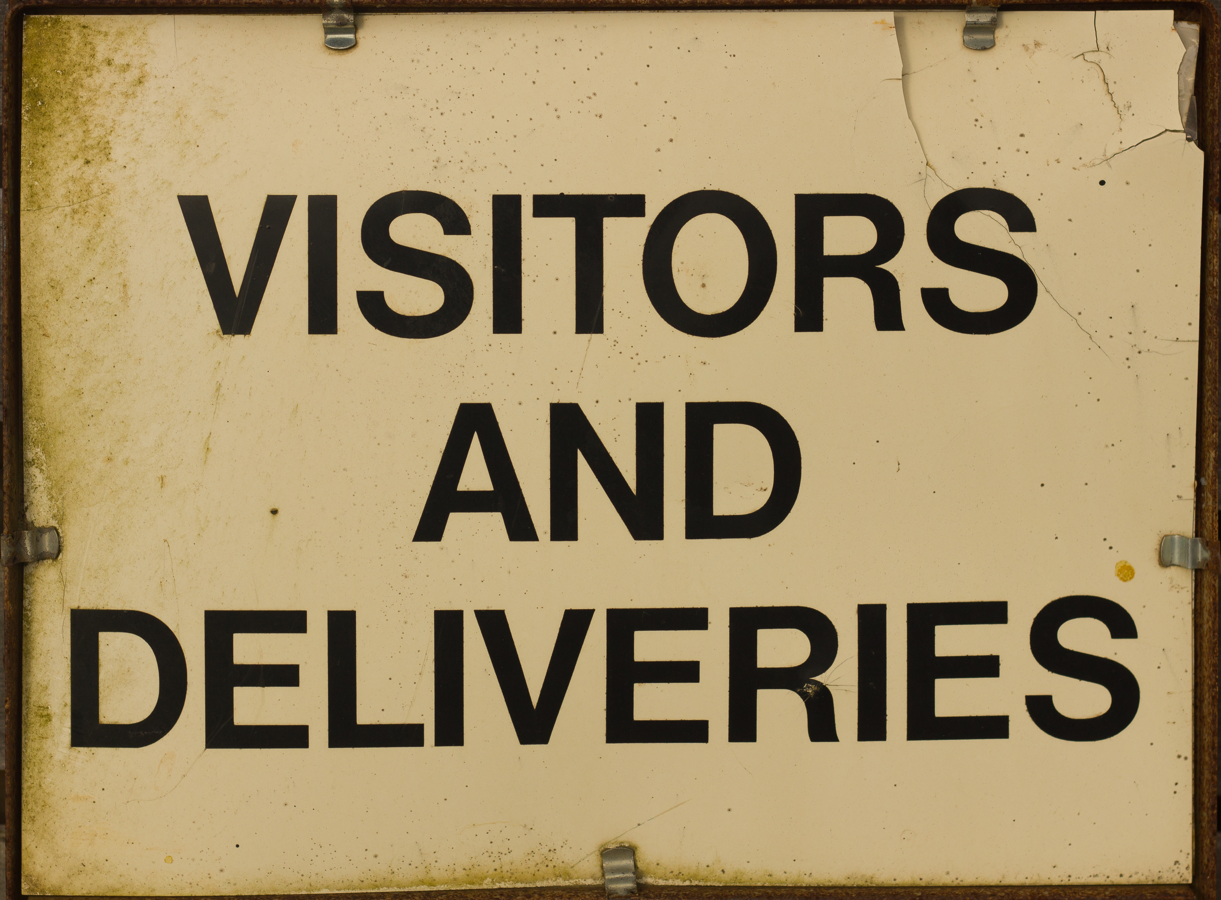 Old tan sign that says Visitors and Delieveries in bold, capital letters.